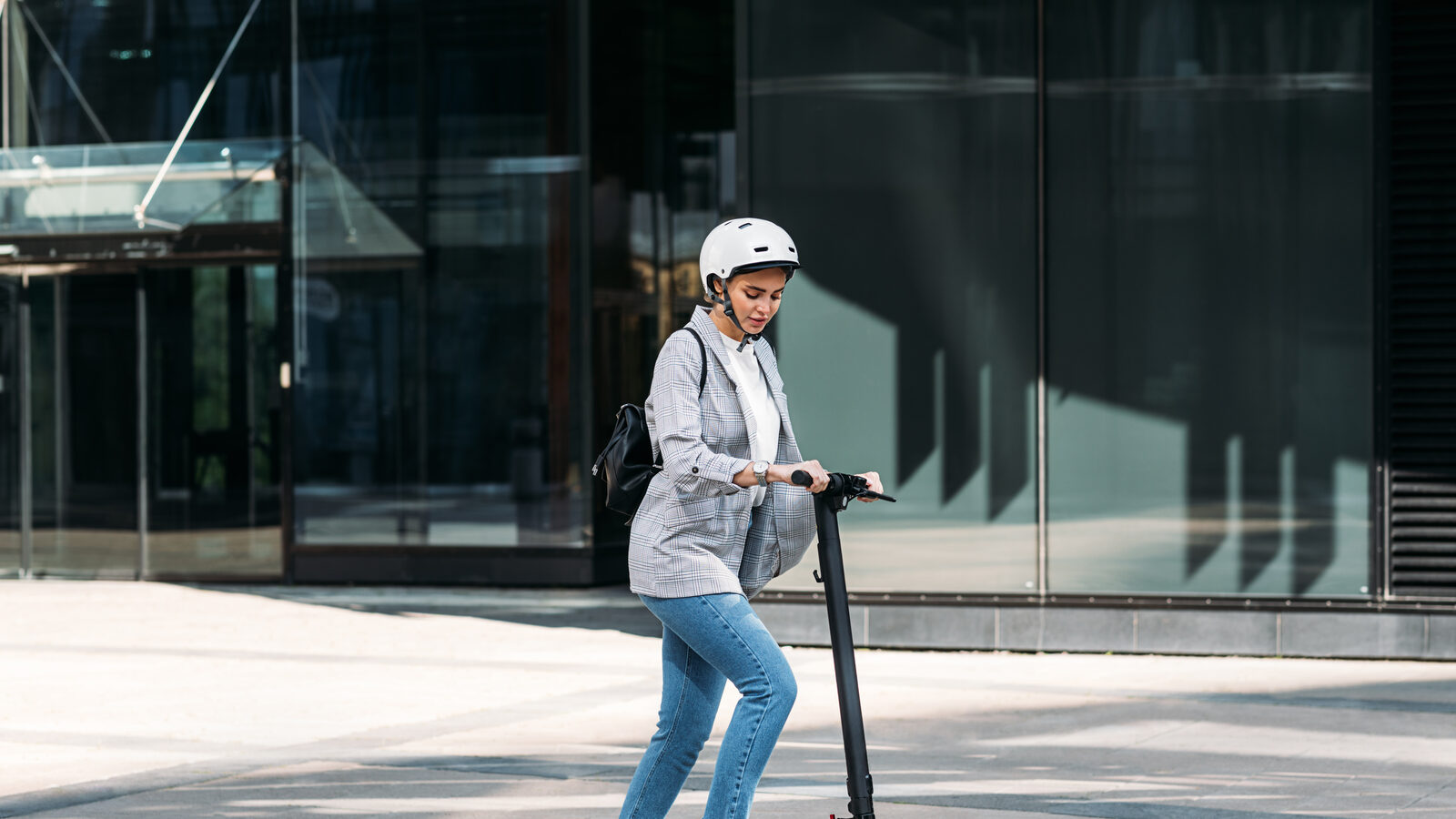 Woman wearing a helmet riding an electric scooter past a glass office building in an Australian city