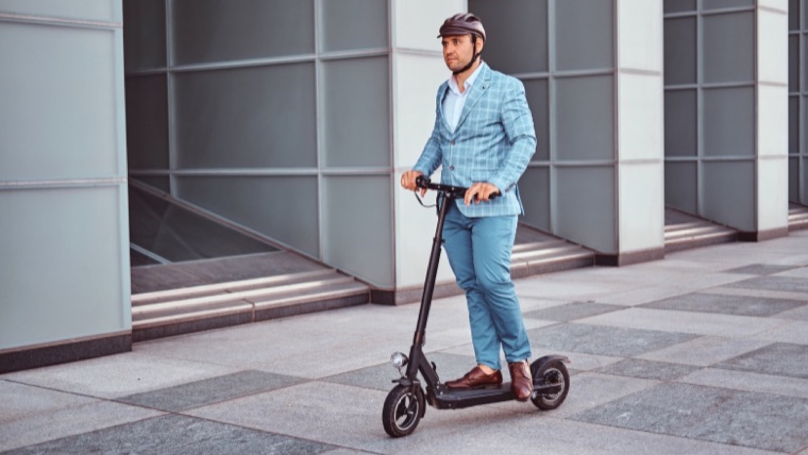 A commuter riding a helmeted electric scooter on a Queensland city street