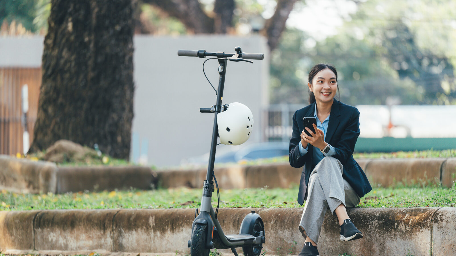 A parked electric scooter on grass, with its owner sitting nearby