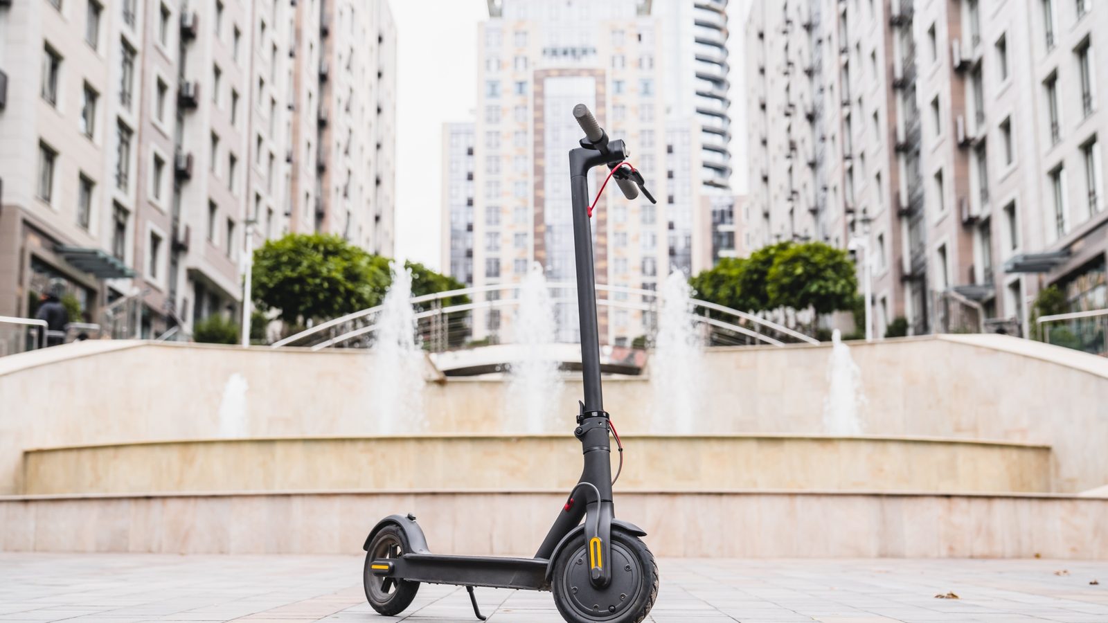 Electric scooter parked on a paved city plaza in front of apartment towers